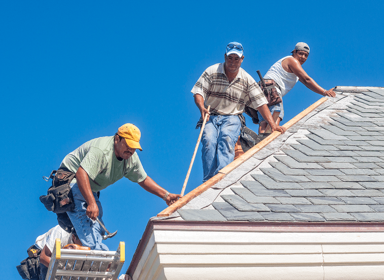 Construction team fixing rooftop shingles.