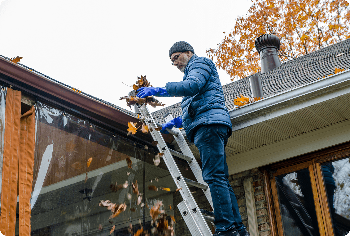 Person removing leaves from roof gutter